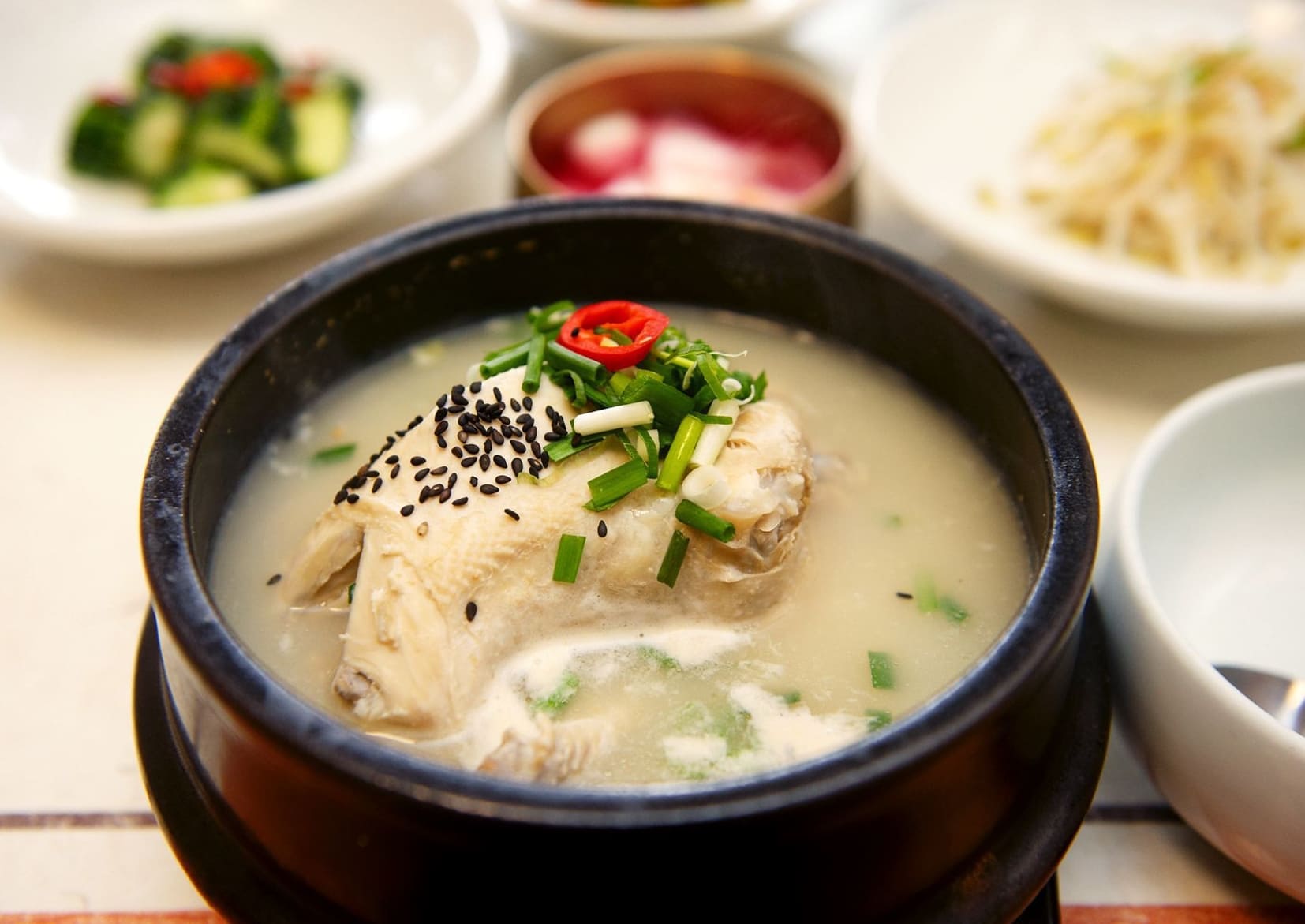 Bowl of samgyetang with chicken, ginseng broth, and garnishes
